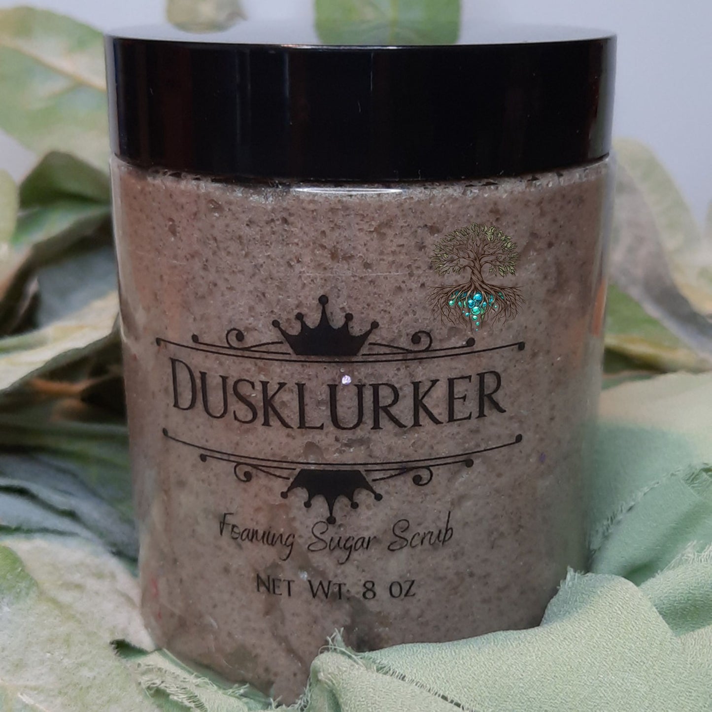 Jar of Dusklurker foaming sugar scrub with a black lid on a green fabric background.