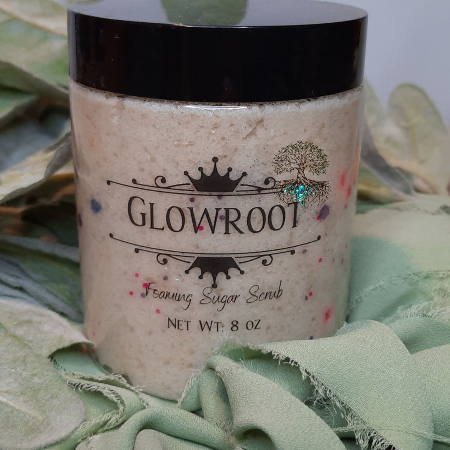 Jar of Glowroot foaming sugar scrub on a green fabric background