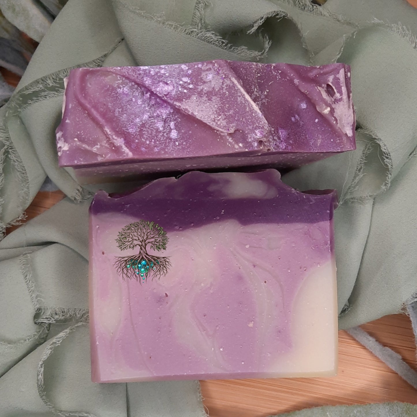 Two purple soap bars with a tree design on a green fabric background