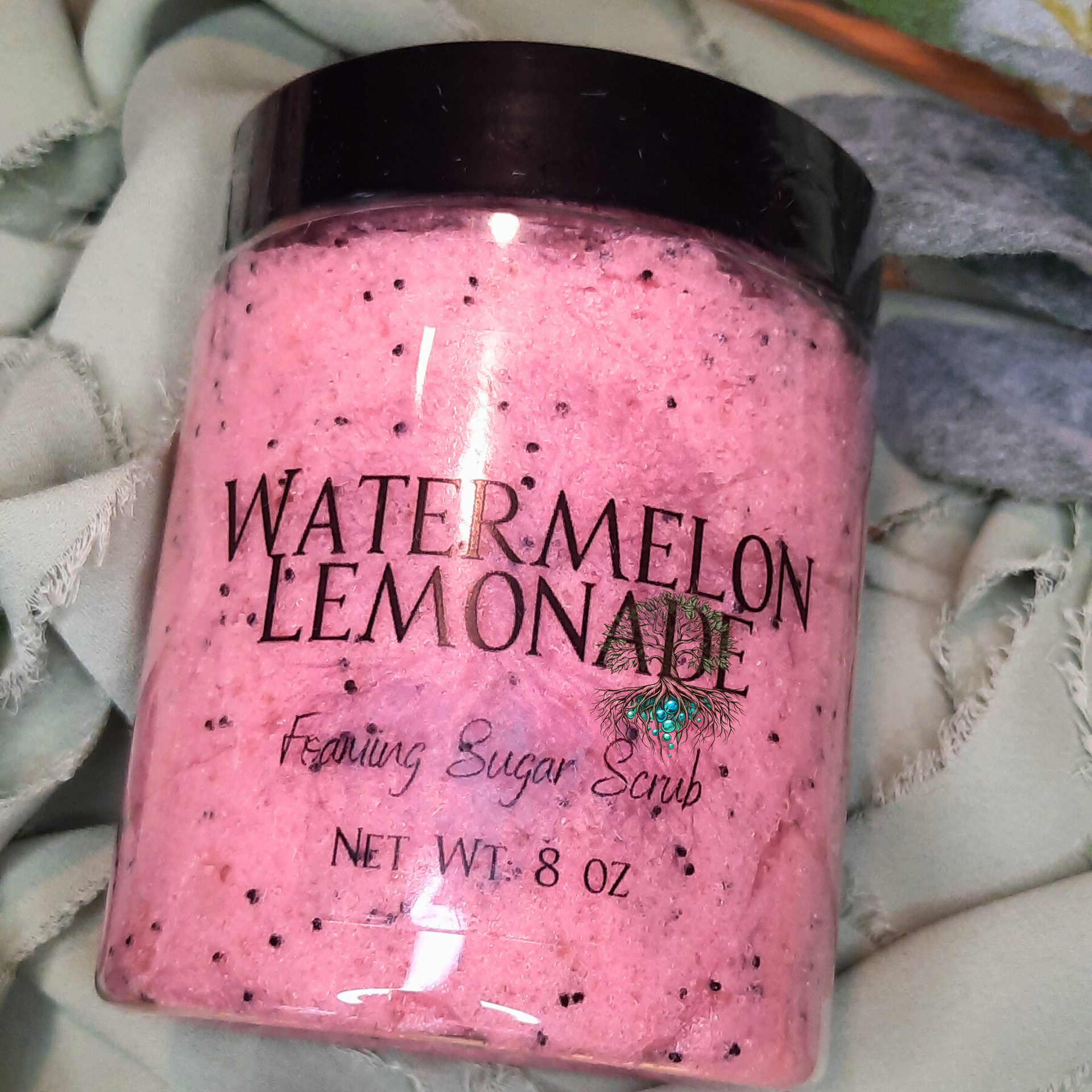 Pink sugar scrub with black lid labeled 'Watermelon Lemonade' on a textured surface.