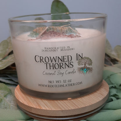 Candle with 'Crowned in Thorns' branding on a wooden coaster with leaves in the background