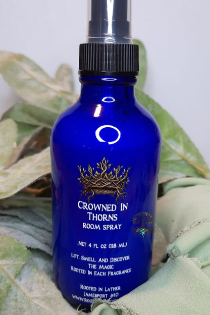 Blue room spray bottle labeled 'Crowned in Thorns' on a green leafy background