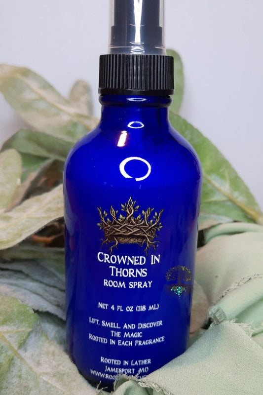 Blue room spray bottle labeled 'Crowned in Thorns' on a green leafy background