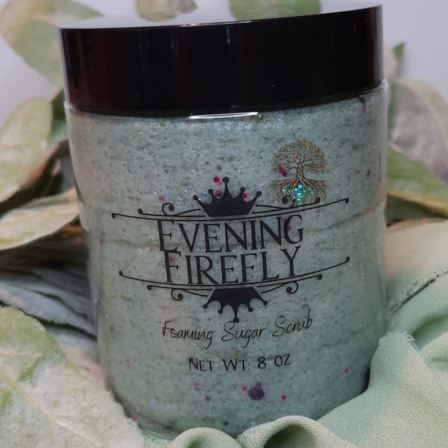 Jar of Evening Firefly foaming sugar scrub with green leaves in the background