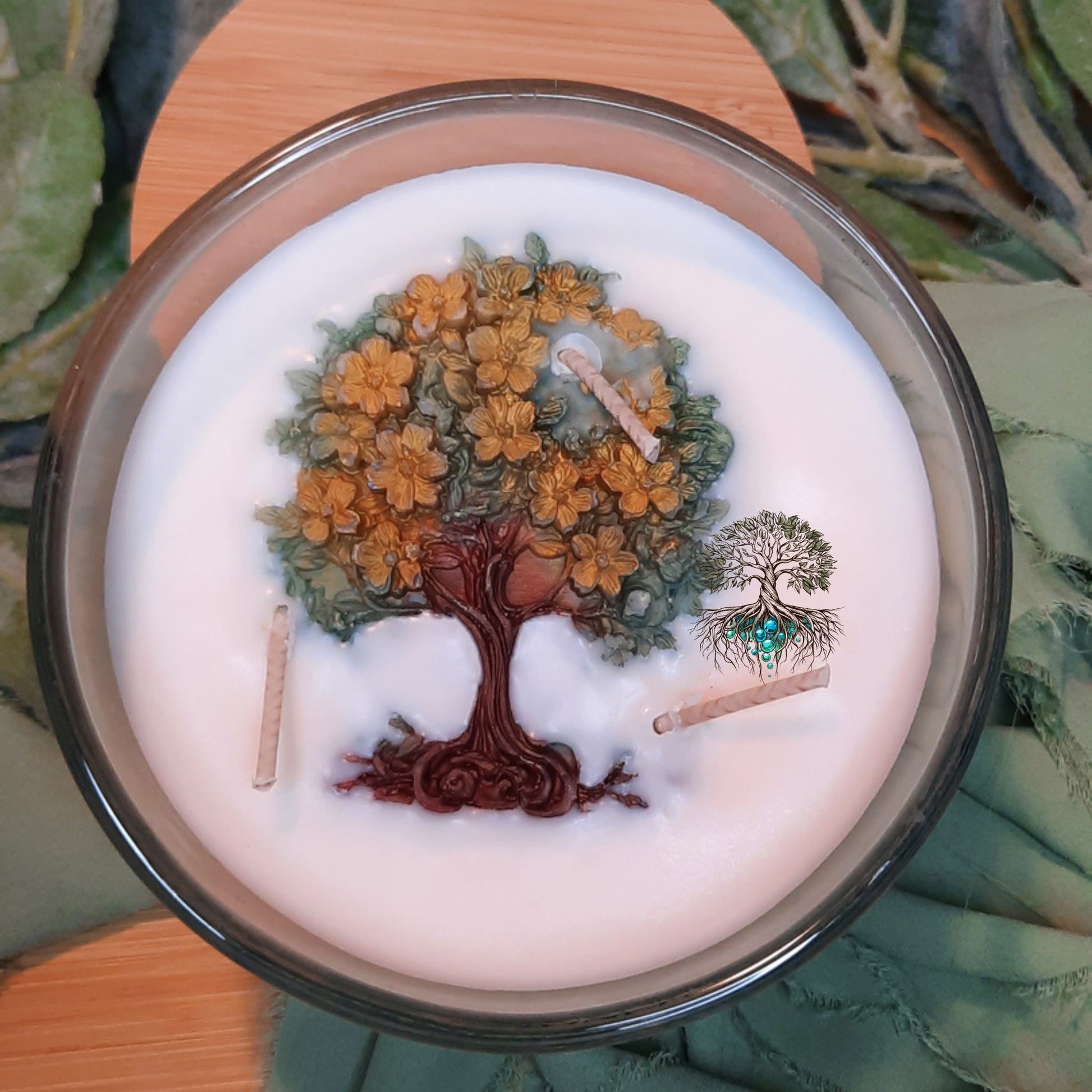 Candle with tree design and small figurines on a wooden surface