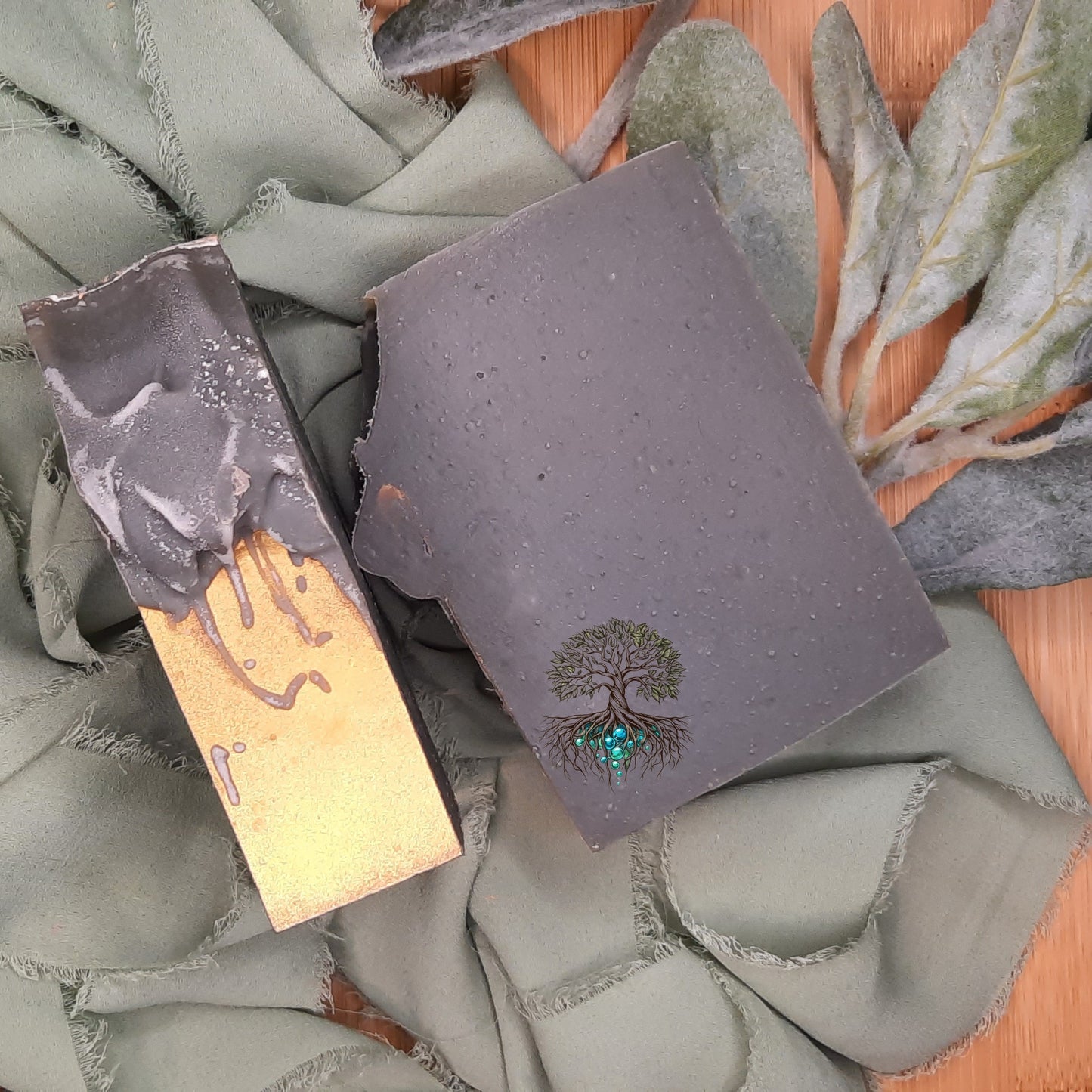 Two pieces of dark soap with tree designs on a textured fabric background