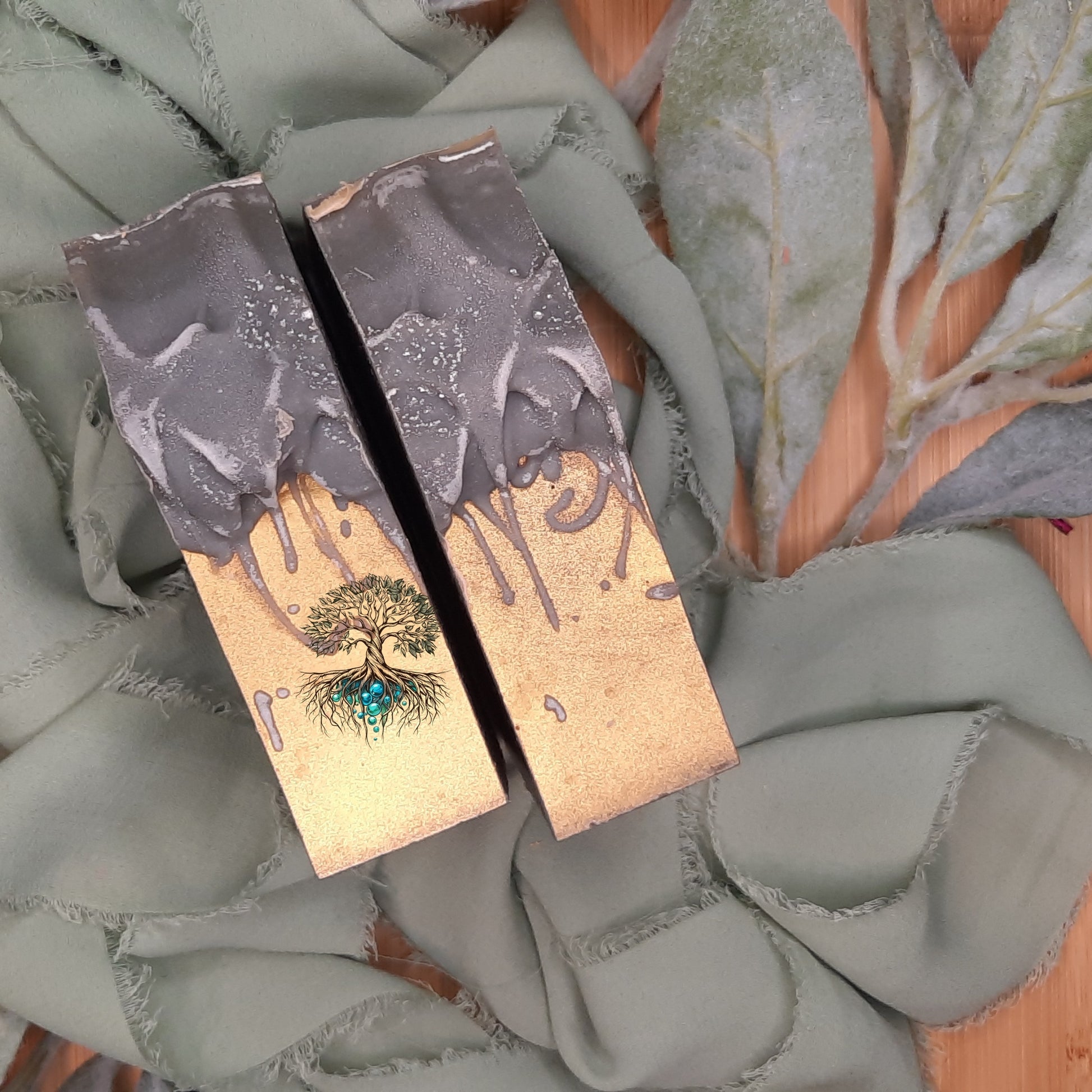 Two grey and gold soaps with tree design on a textured surface