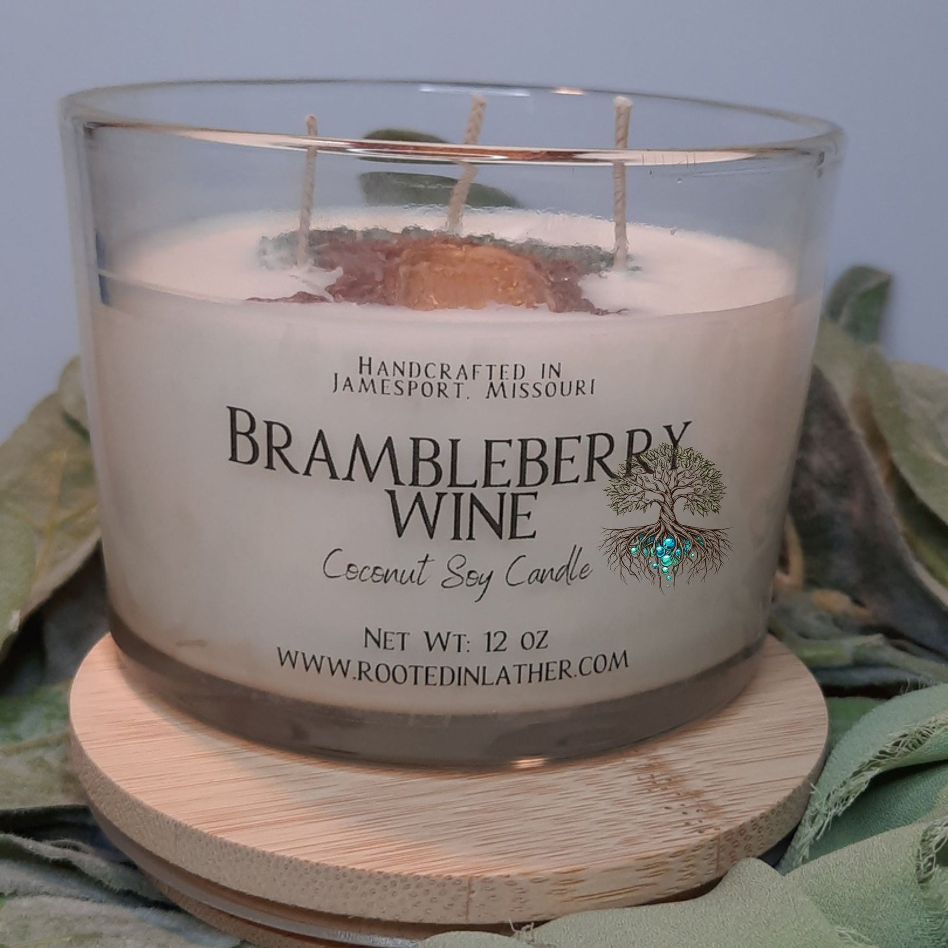 Candle labeled 'Brambleberry Wine' with a wooden coaster on a leafy background